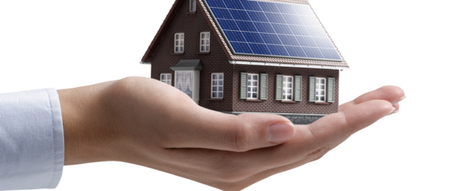 Hand holding a model house with solar panels, representing Sunergy Systems' commitment to sustainable residential solar energy solutions.